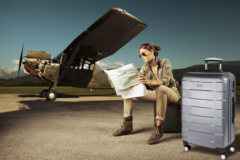 Beautiful young woman sitting on a suitcase, looks at a map. Airplane in the background